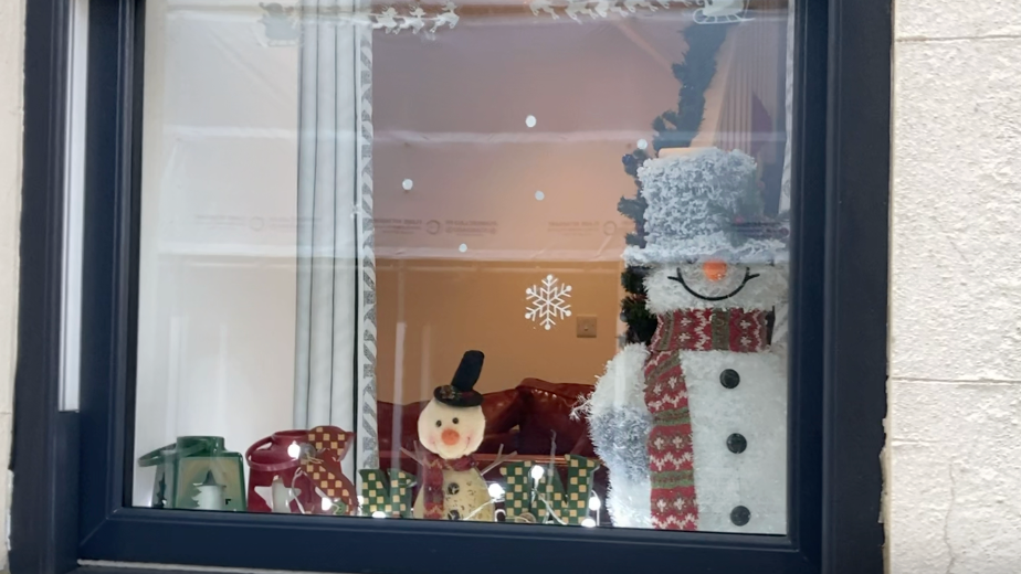 A Christmas window decoration featuring two snowmen, a green and red lantern and snowflakes printed onto the window pane.