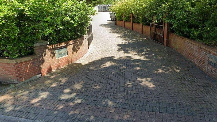 The entrance to a small, unpaved road with low brick walls on either side and green laurel hedges. There is a plaque on the wall that says Grove Place