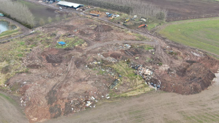 A drone image of an illegal waste site, showing a brown patch of land with waste products dotted around the site.