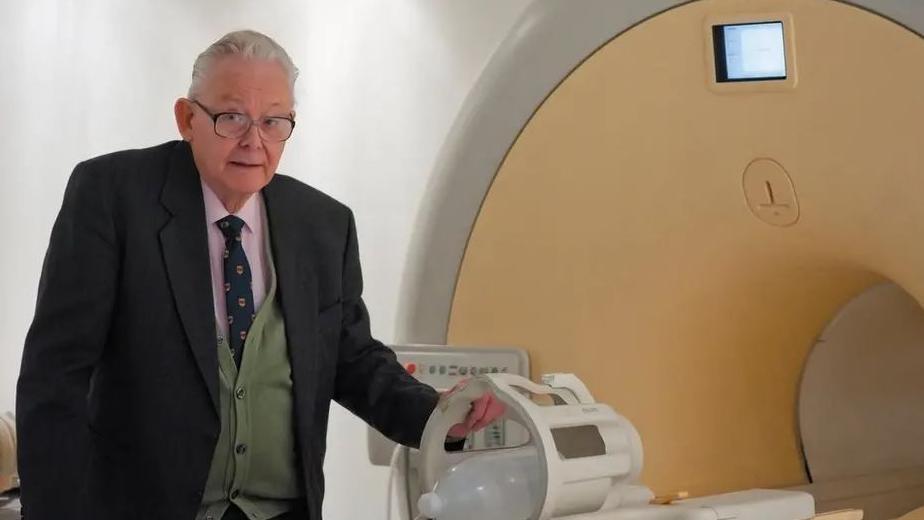 Sir Peter Mansfield standing next to an MRI scanner