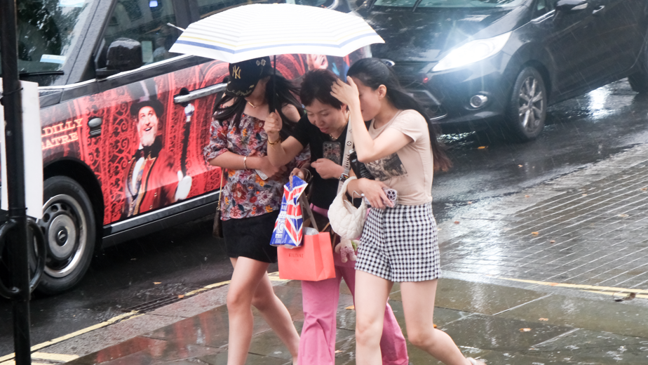 Three women walk under an umbrella during a rainstorm in London