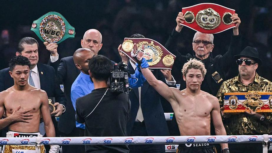 Naoya Inoue holds up his arm as the super-bantamweight world titles are held up behind him