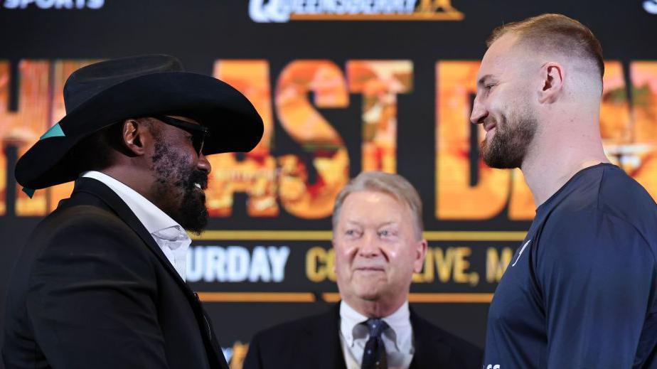 Derek Chisora in a cowboy hat smiles and faces off with Otto Wallin