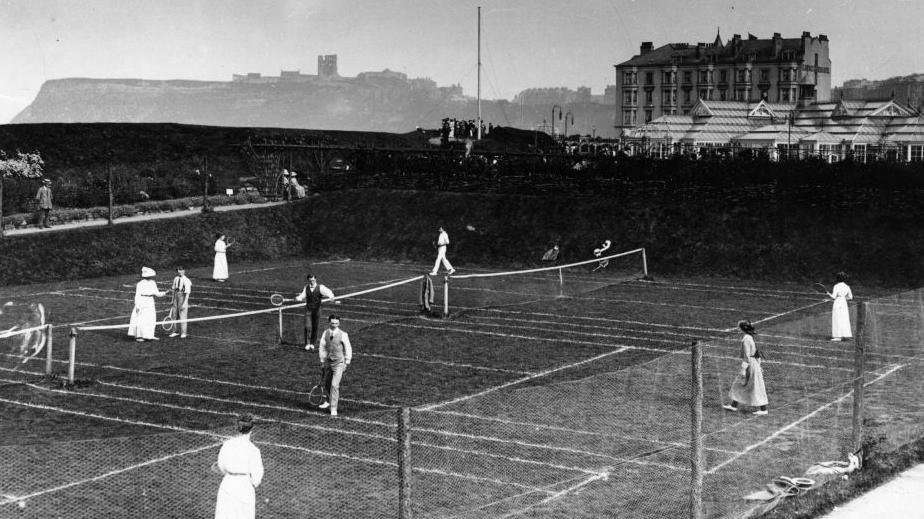 People playing tennis at Scarborough in about 1913. The Floral Hall, a large glass building is behind the tennis courts.