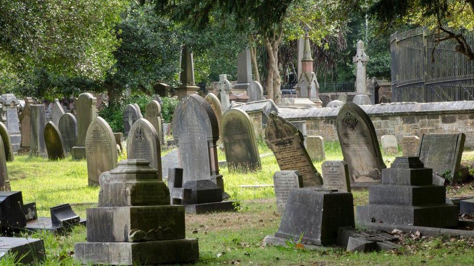 A number of stone monuments and gravestones, some of which are leaning forwards