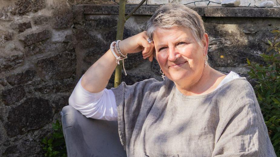 Amanda Greenwood is wearing a grey top over a white t-shirt