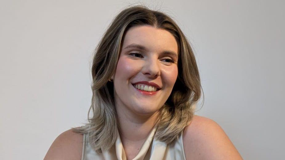 Jess Warren in a cream, sleeveless blouse, smiling and looking away from the camera.