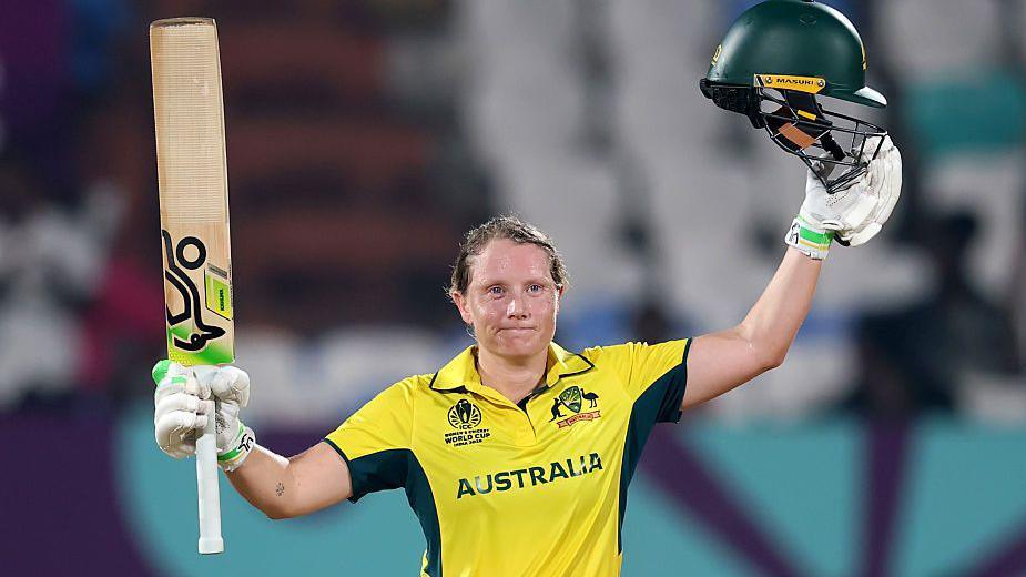 Alyssa Healy holds up her bat and helmet