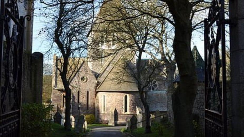 The exterior of the church showing gravestones and trees leading up to it.