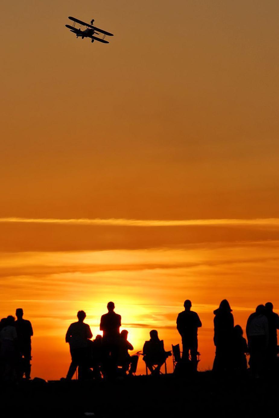 People watching a biplane at Ayr Festival of Flight, silhouetted against a sunset