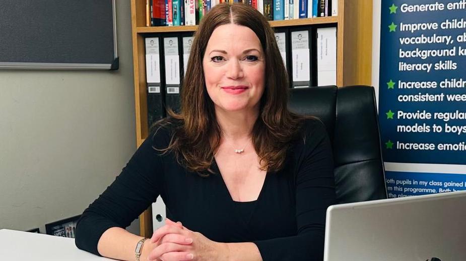 Sonia wearing a black top sitting at a desk, smiling at the camera