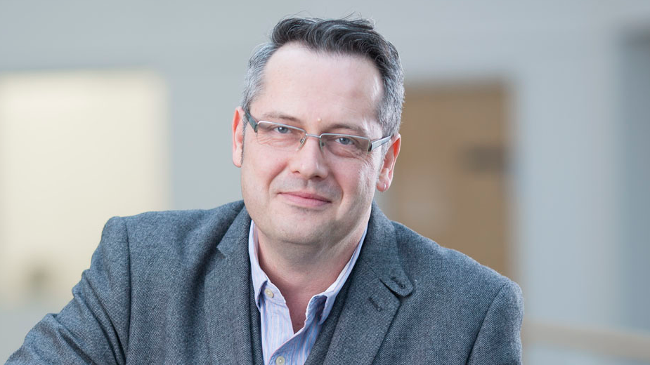 Professor Richard Bowden from the University of Surrey. He is wearing a pale blue shirt and grey suit jacket. He is looking to camera and has greying hair and grey-framed glasses.