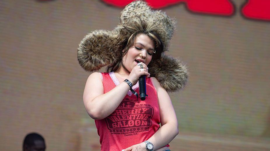 lola young singing on stage in a big fluffy hat