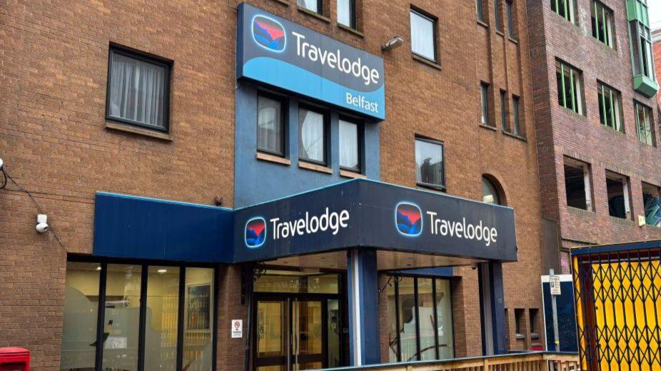 Outside view of Travelodge in Belfast city centre. The building is brown bricked and the Travelodge sign is blue with white writing.