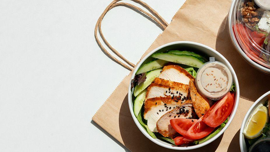 A takeaway salad in a paper bowl on a brown paper bag with wooden fork