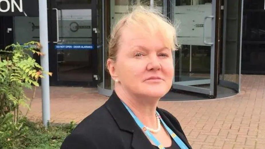 Norfolk Coroner Yvonne Blake dressed in a black top with blue lanyard and necklace, near a set of revolving doors