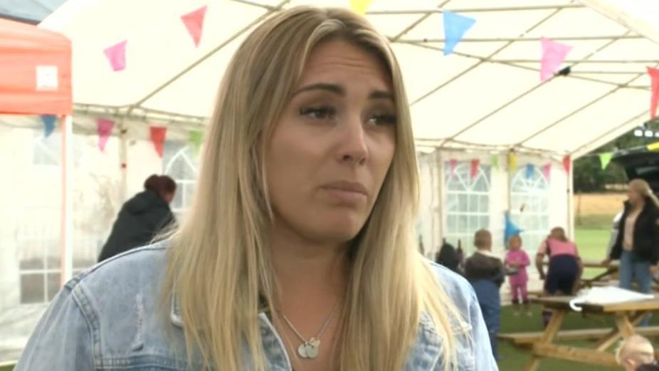 Mrs Gray wears a light denim jacket and is looking off camera in a marquee with bunting hanging from the ceiling