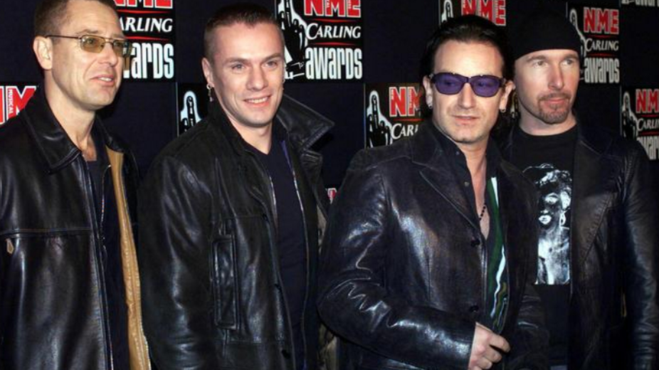 Adam Clayton, Larry Mullen, Bono and The Edge from U2 in a photograph from 2001. They are standing in front of a sponsorship backdrop for the NME awards.