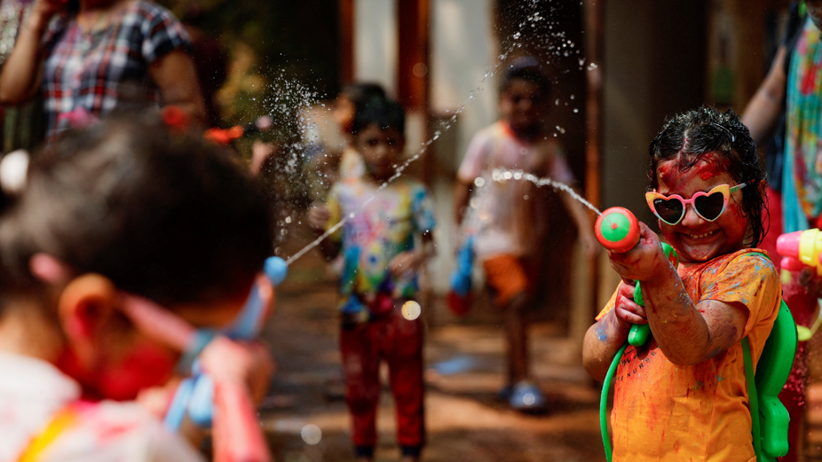 A girl wearing heart-shaped sunglasses smiles brightly as she sprays her friend with water