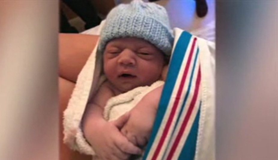 An image of a baby in a blue knitted hat wrapped in a blanket. 