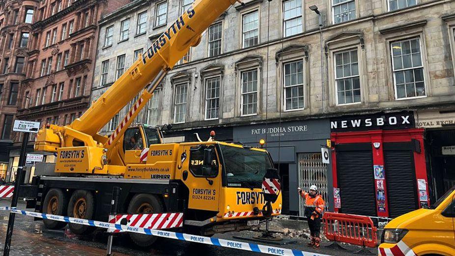 A construction crane with police tape around it, working on secure a building where stonework has fallen from