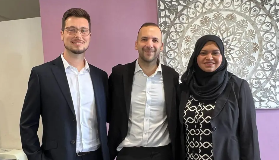 Three people stand close together smiling at the camera. Two men, Tom Butcher and Zack Polanski, are in black suits with open-neck shirts, while Repi Begum is on the right, wearing a black blazer with a patterned top.
