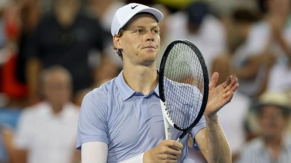 Jannik Sinner holds up his tennis racquet