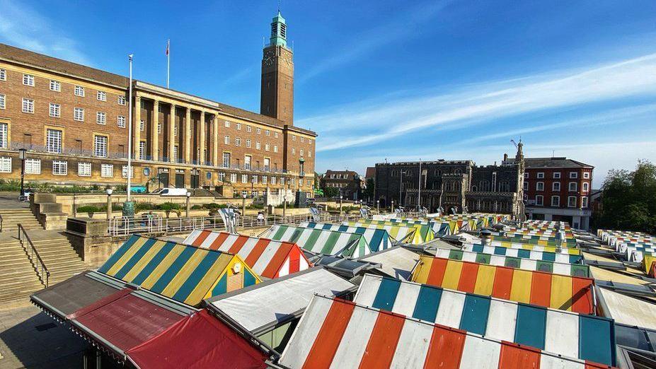 Colourful market stall roof tops with Norwich City Hall and the Guildhall in the background.