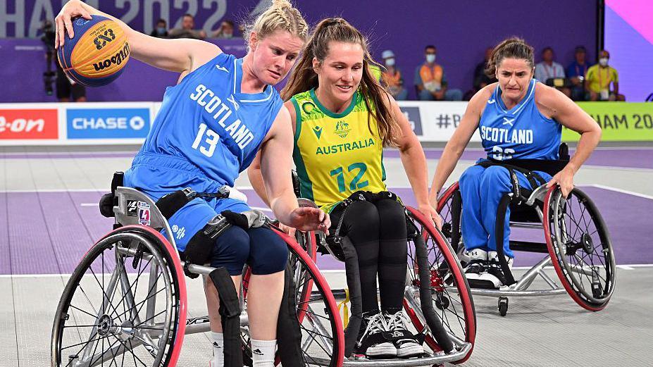 Three players in wheelchairs with Scotland's Robyn Love (left) in blue holding the ball in her outstretched right hand as she is challenged by Australia's Georgia Inglis in yellow.
