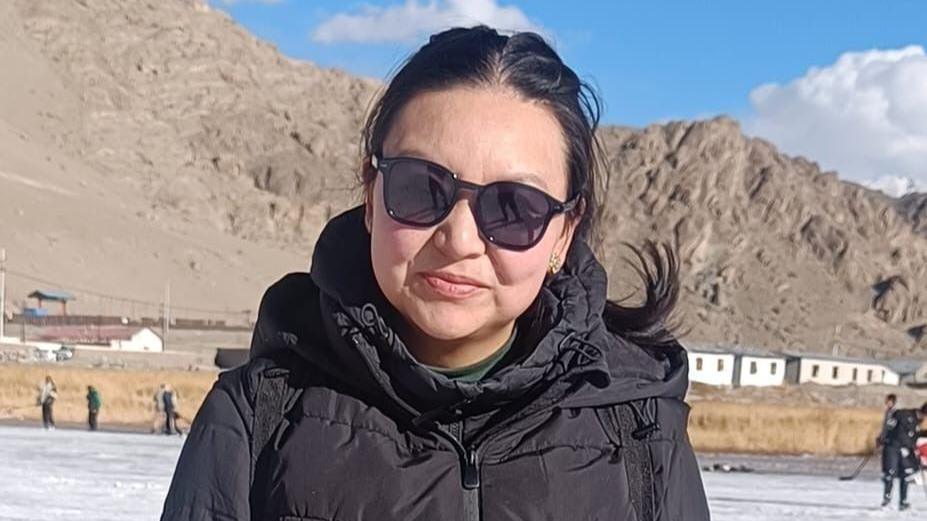 Deskit Angmo, the head of the women's wing of Ladakh Buddhist Association, stands in front of mountains wearing a black jacket and sunglasses.
