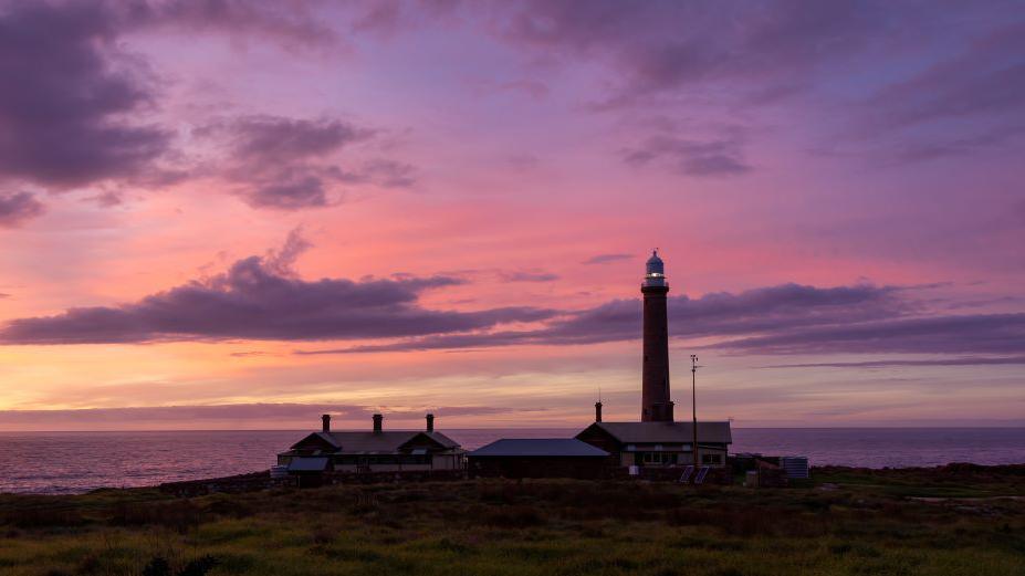 Gabo Island lighthouse, tall structure under a purple sunrise sky, with the sea also in the background.