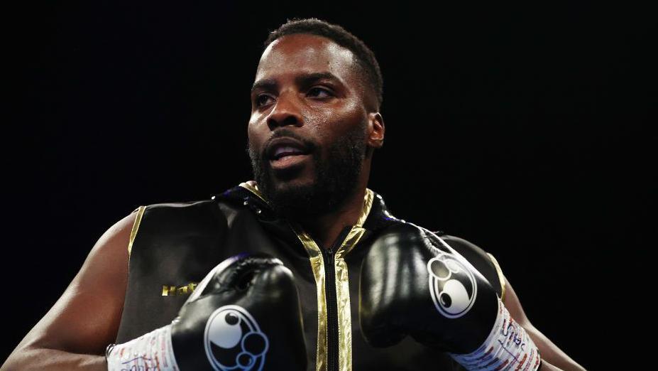Lawrence Okolie in black boxing gloves and sleeveless black and gold zip-up top