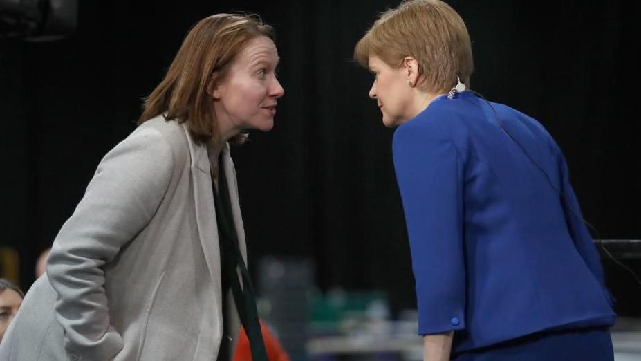 Mae'r llun yn dangos Liz Lloyd - menyw ifanc - yn sgwrsio gyda Nicola Sturgeon