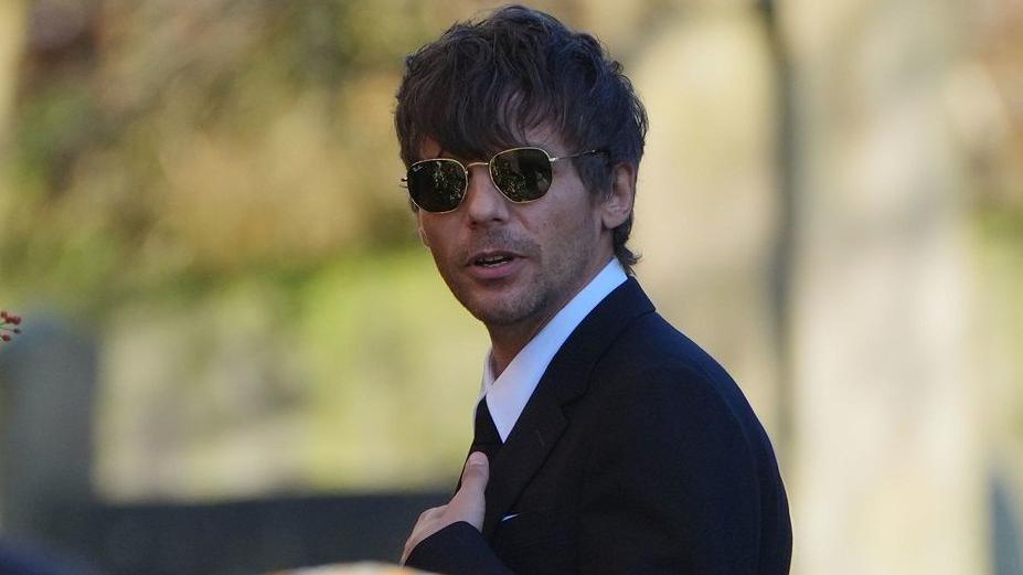 Louis Tomlinson pictured outside the church in a smart dark suit and shades