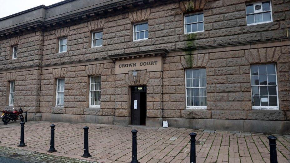 A general view of a sandstone building with a paved area in front of a doorway, over which is a sign reading 'Crown Court'.