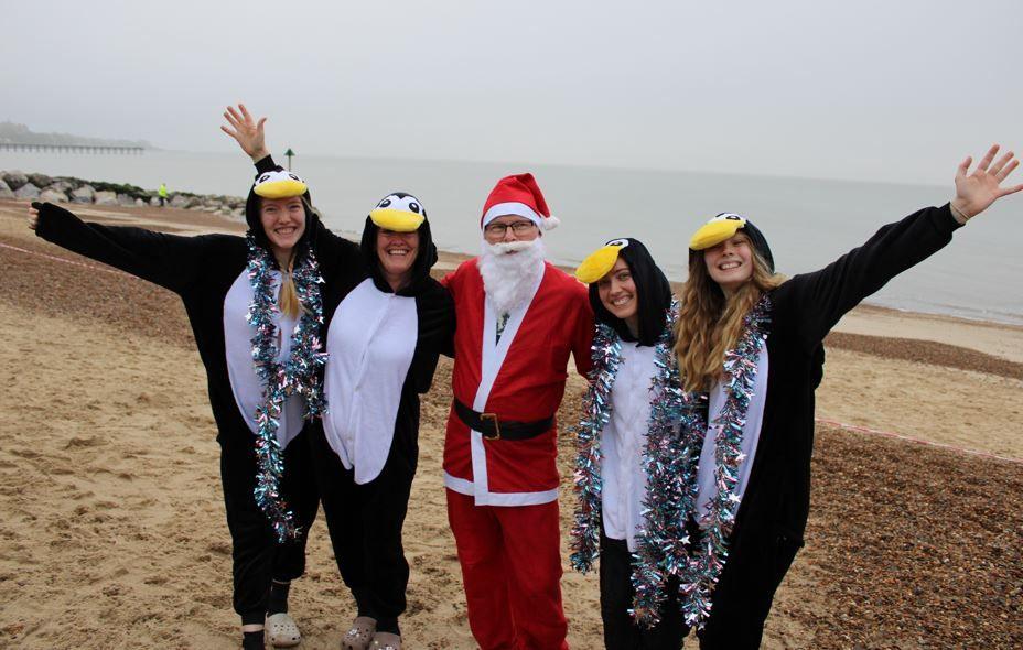 Four people dressed in penguin outfits on Felixstowe beach, with a person in a Father Christmas outfit in the middle