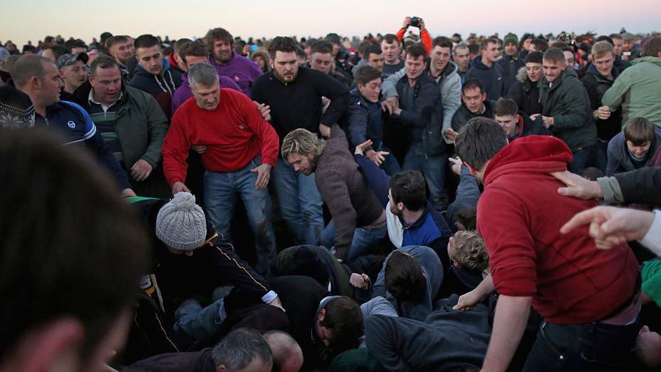 A large group of men and boys battling for the leather "hood". Some are on the ground, while others surround them.