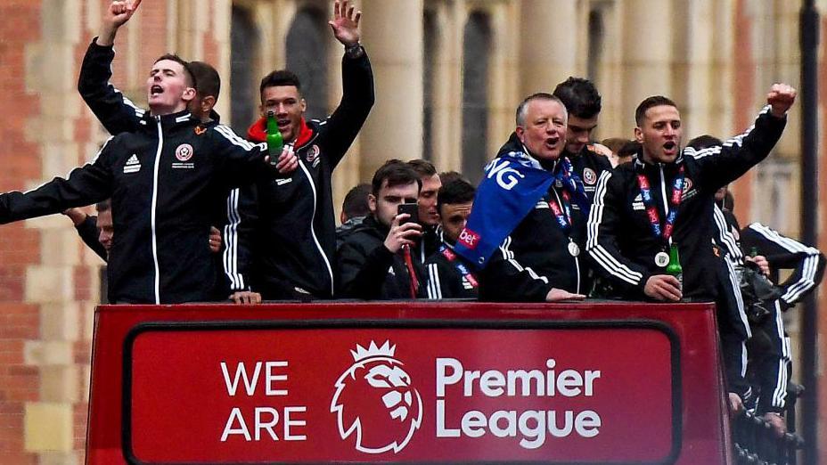 Chris Wilder and Sheffield United players on an open-top bus, celebrating above a banner saying 'We are Premier League'