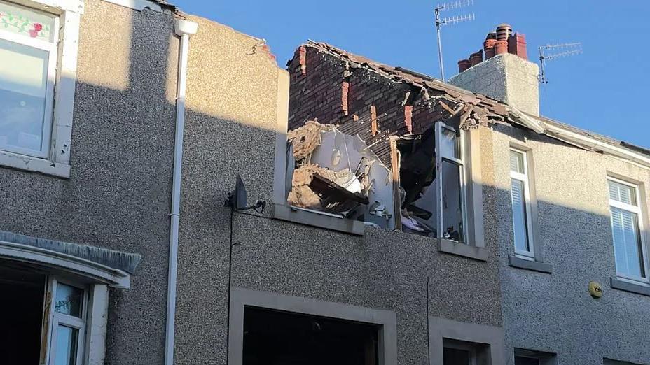 The upper part of a damaged building which has a wall and part of its roof missing. 