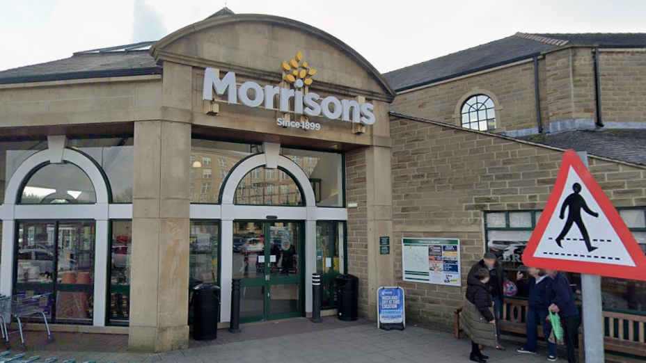 The exterior of a stone-built Morrisons supermarket with shopping trolleys lined up outside.