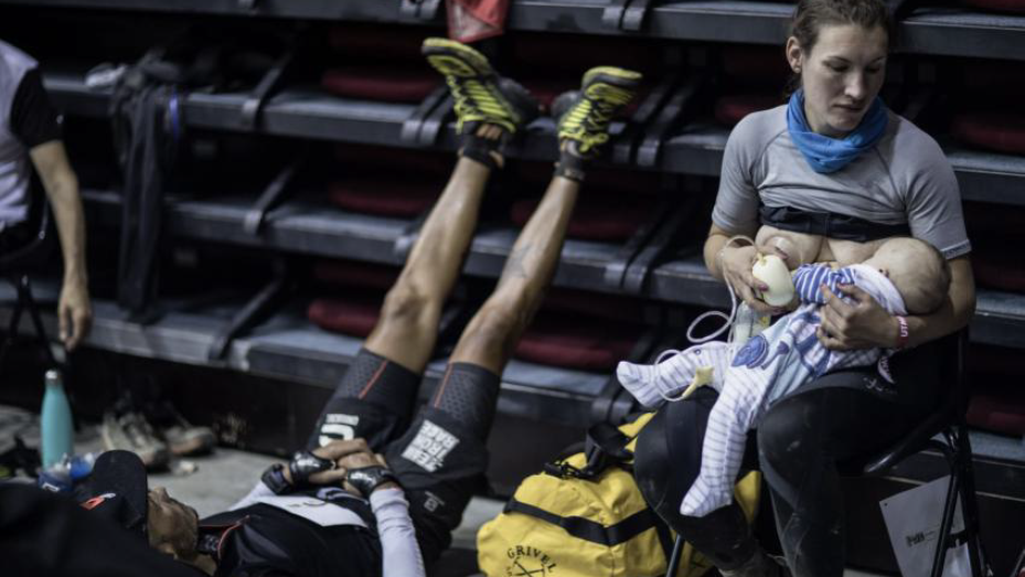 Sophie Power in a photo sat breastfeeding her baby. On the left of her is a man who is also a runner lying with his legs up.