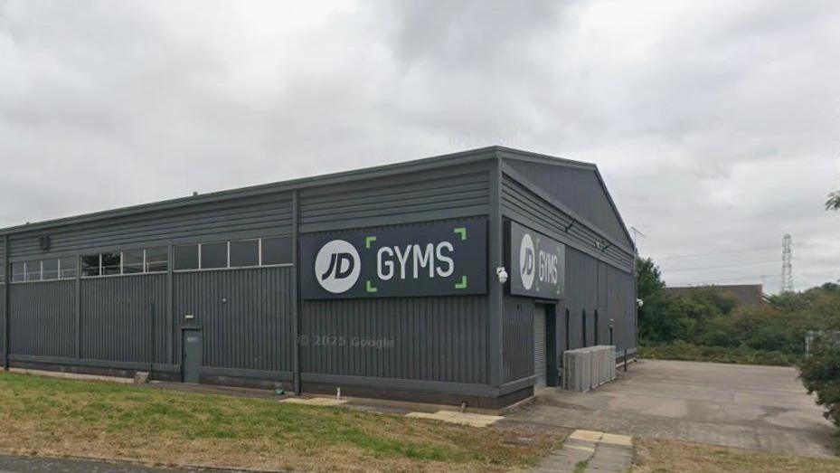 The side of a grey building with corrugated metal sides and a large sign which reads JD Gyms