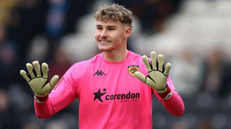 Carl Rushworth, in his pink goalkeeper shirt, puts his hands out in a calming manner to his defenders during a match for Hull City