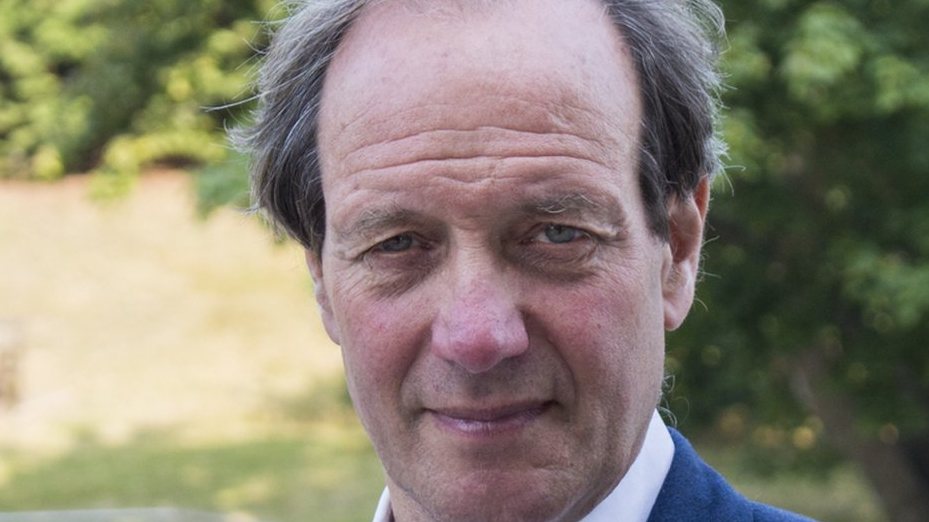 Andrew Jamieson looking directly at the camera. He is outside on a sunny day with foliage in the background.