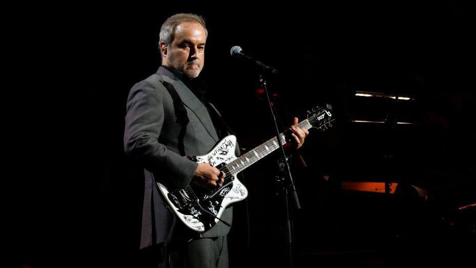 David Arnold playing a signed white electric guitar on stage