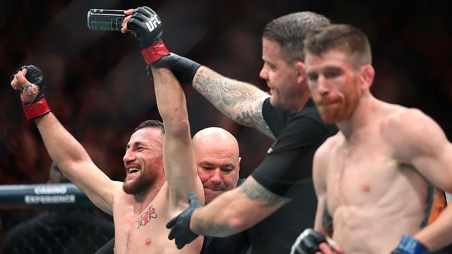 Merab Dvalishvili smiling as the referee raises his hand with Cory Sandhagen looking on