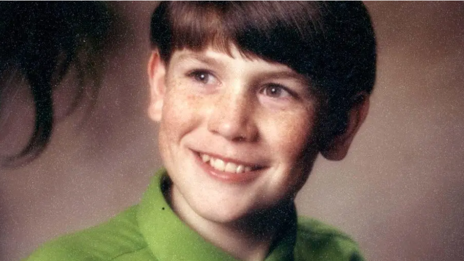 Headshot of a young boy wearing a green shirt and smiling while look off camera.