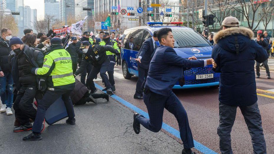 Police attempt to stop demonstrators running in front of a car containing Yoon