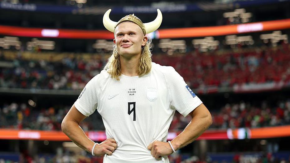 Erling Haaland está de pie con las manos en las caderas, sonriendo y con un casco vikingo en la cabeza.