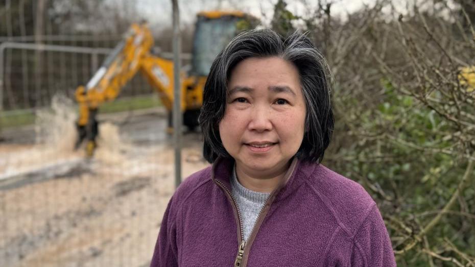 Image of Nisih - she is stood in front of some fences put up by Severn Trent with a digger working on the water leak